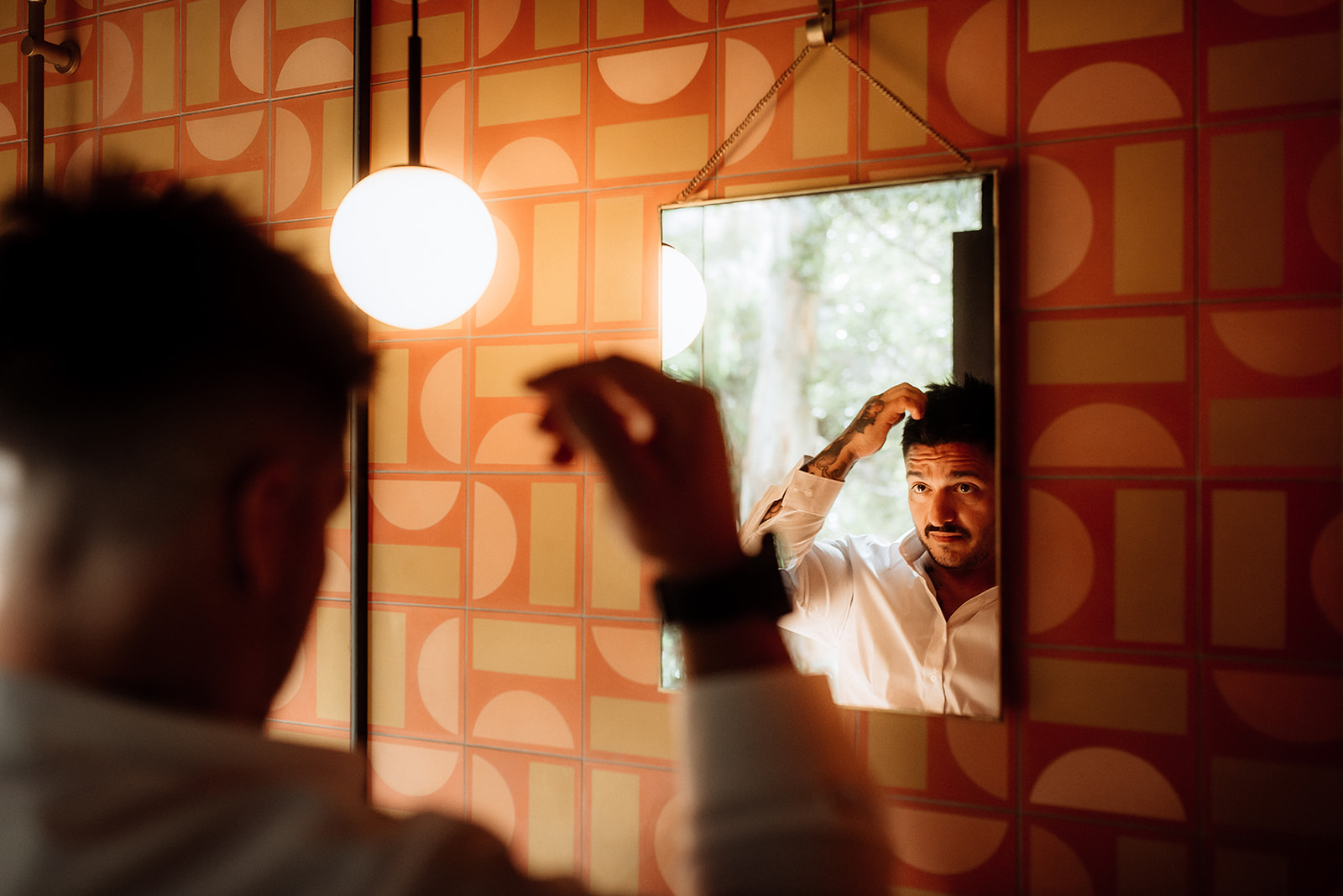 A groom fixes his hair in the mirror as he gets ready for his wedding day elopement in Tasmania