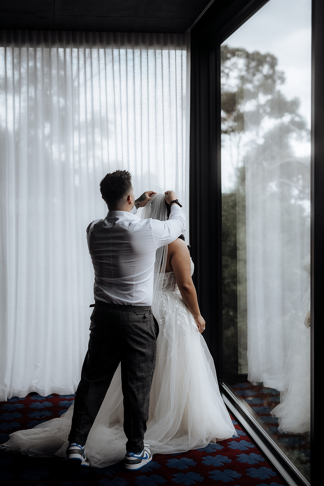 A groom fits the bride's veil as they are getting ready for their elopement in an Airbnb in Hobart, Tasmania
